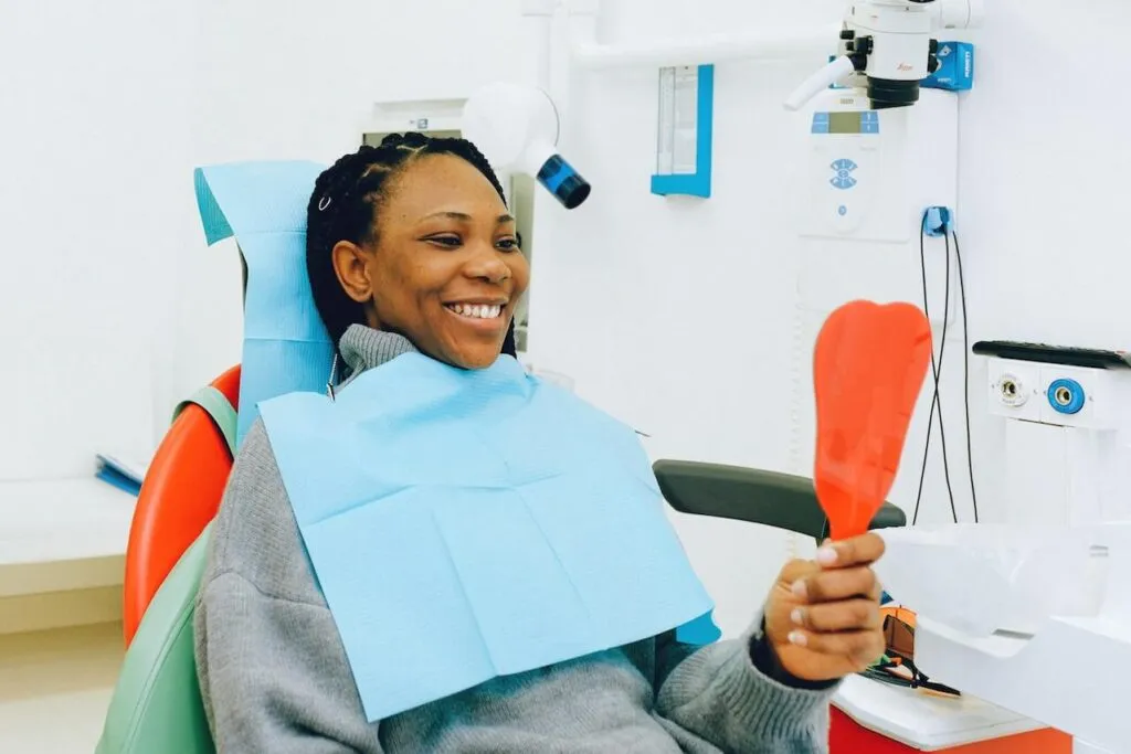 A woman at her dentist office holding an orange mirror to check her teeth