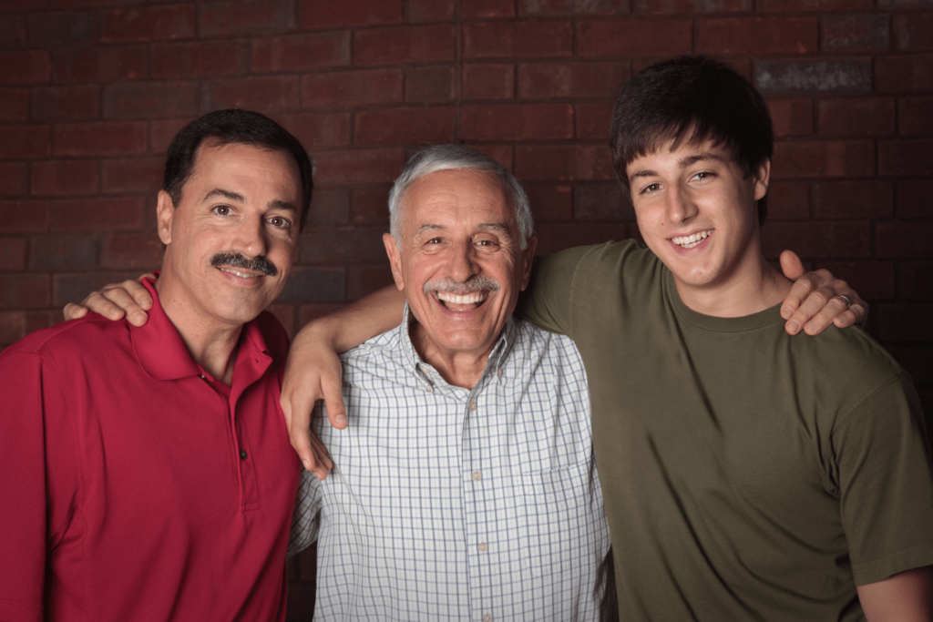 Is Prostate Cancer Hereditary? 3 males standing besides on another, each putting their hand over the next one's shoulder. All 3 are smiling and look happy.