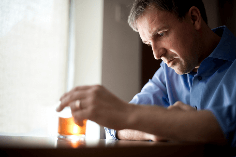 A man in a blue shirt has an alcohol drink in front of him. He's pondering whether he should have that drink. Even 1 alcohol drink does raise blood pressure, after all!