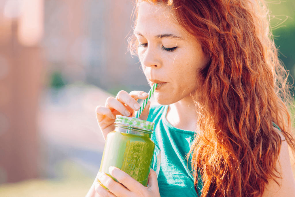 A red-haired female sipping on a green smoothie using a paper straw which contains high levels of the forever chemicals.