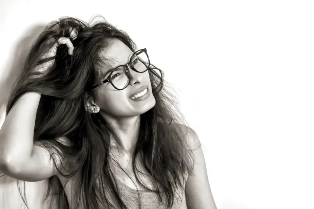 A girl with glasses scratching her long black hair due to dandruff