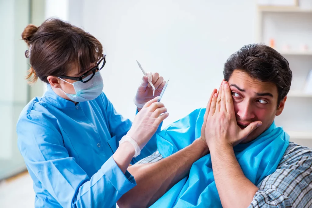 A man at his dentist visit covering his mouth with his hands indicating that he's scared of the dental procedures.