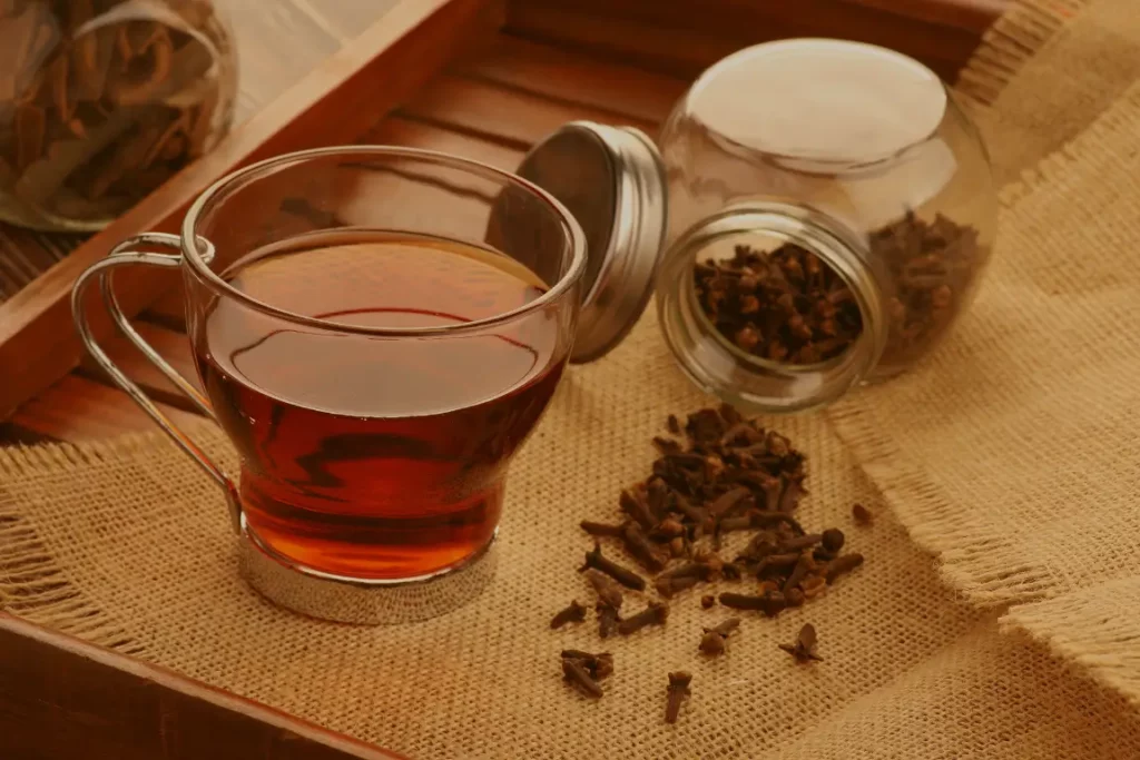 Clove water in a cup on a table besides a jar of cloves